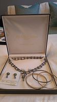 Photo of the full jewelry set inside open box showing necklace, earrings on card, and two metal bracelets.