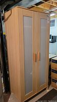 Full view of the Ikea wardrobe showing two doors with frosted glass panel inserts and pine-like finish, located in a basement environment.
