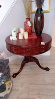Full view of the round wood occasional table showing the leather inlay and gold leaf top with several candles and vases placed on it
