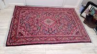 Full view of rug laid on floor showing overall red floral pattern and fringe