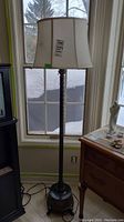 Full view of the standing lamp showing the metal base and fabric shade near a window.
