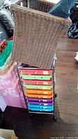 Full view of metal framed storage unit featuring multiple colorful plastic drawers and casters, with wicker basket on top and adjacent storage boxes.