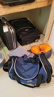 Overall view of the luggage and travel items including black wheeled bag, duffel bag, travel pillow and cloth item
