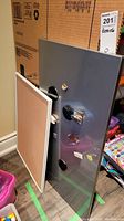 Magnetic board with round and rectangular magnets attached leaning against a cardboard box, alongside cork board with wood trim also leaning.