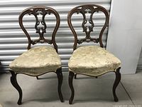 Pair of antique handcrafted wooden chairs with carved backs and upholstered seats showing front view placement side by side
