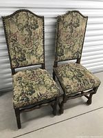 Pair of antique Louis XVI-style side chairs, front view, showing arched padded backs and detailed tapestry upholstery with landscapes and foliage patterns.