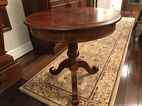 Front side view of the round pedestal table showing the turned column and curved legs on a patterned rug.