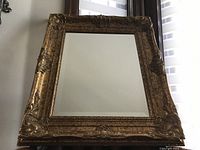 Front view of vintage rectangular mirror with thick gold ornate frame showing embossed foliage and carved decorative corners.