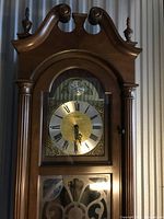 Upper front view showing swan neck pediment, finials, brass dial with Roman numerals and decorative spandrels.