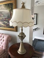 Front view of brushed brass table lamp with ornate base and cream fabric scalloped edged lampshade with beige trim