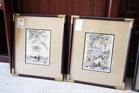 Two framed oriental ink drawings leaning against wooden surface with carpet floor.
