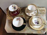 Four vintage tea cups and saucers on marble surface showing front view and floral details