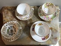 Top-down view of four tea cups on matching saucers, showcasing floral and crest designs