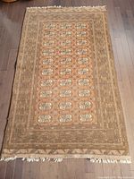 Full view of the rectangular Bokhara wool rug laid flat on dark hardwood floor showing overall design and tassels on shorter edges.
