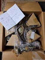 Photo showing chandelier parts in an open box, including metal parts wrapped in plastic and detailed instruction manual.