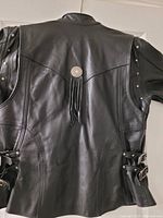 Back view showing black leather with a concho and tassel detail, and buckle adjustments on the sides.