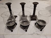 Side view of three brown metal candle holders with three glass votive holders in black metal bases on white tiled floor.
