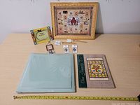 Photo shows the gift lot arranged on a table including the framed cross-stitch piece, scrapbook album, family tree book, two keychains, wooden bookmark, and pen.