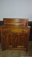 Front view of antique wooden washstand showing drawer and cupboard doors.