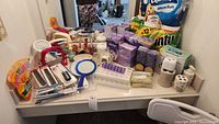 Wide view of assorted bath and sanitary items including toilet paper, hand mirrors, combs, toothbrush holders, soap dispensers.