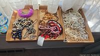 Overview of assorted costume jewelry including multiple necklaces in various styles and colors displayed in three cardboard trays.
