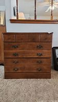 Front view of the chest showing 3 small drawers on top and 4 larger drawers below with metal handles, polished wood surface, standing on carpet.