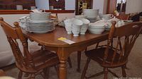 Full view of the maple dining table with plates and cups on top and four wooden chairs around it.