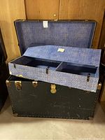 Full view of open large vintage steamer trunk showing blue patterned fabric lining and removable tray compartments inside.