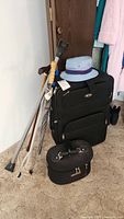 Image showing black rolling suitcase, canes, umbrella, and blue bucket hat