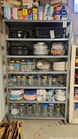 Front view of metal shelving unit with seven shelves and various household items stacked on it, including glass jars and pans (contents not included).