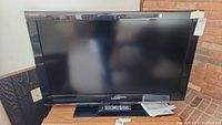 Full front view of Samsung flat screen television on base stand with remote and papers on stand surface