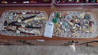 Tray with varied wristwatches mostly analog with metal, leather, and expansion bands, alongside several costume brooches in multiple styles and colors.