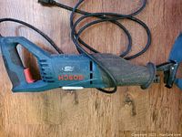 Bosch 120V corded reciprocating saw lying on wooden floor showing overall body, handle, motor vents and power cord