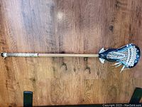 Full view of the old style lacrosse stick with wooden shaft and Brine STX head showing the overall length and grip.