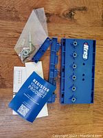 Kreg blue plastic shelf pin jig with five holes, adjustable stop collar, screws, and instruction manual shown on wood surface.