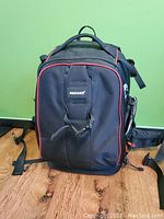 Front view of black Neewer camera backpack with red trim on wooden floor against green wall.