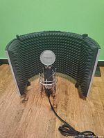 Front view of Marantz condenser microphone set inside Neewer NW-5 acoustic foam sound screen on wooden floor against green wall, with cable coiled in front.
