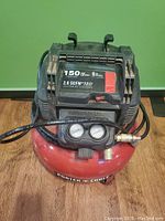 Front view of Porter-Cable compressor showing red tank, black motor housing, carry handle, and attached black coiled hose.