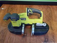 Front and side view of the Ryobi One+ cordless portable bandsaw with lime green and black body. Tool is cordless with ergonomic handle and trigger.