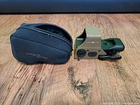 Sightmark laser sight and its carry case placed side by side on wooden surface, showing both items and their relative size