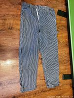Full view of a pair of blue and white striped pants laid flat, showing the tapered leg design and overall condition of the fabric.