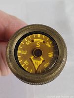 Top view of the compass showing yellow face with N, S, E, W and intercardinal directions, brass casing visible.