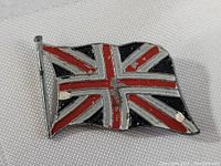 Close-up front view of antique British Union Jack flag pin showing scattered enamel wear and chipping on the painted flag design.