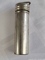 Front view of vintage metal cylindrical match holder with vertical engraved lines.