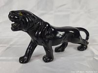 Full side view of a glossy black panther figurine with walking pose, showcasing the figure's smooth resin surface and detail.