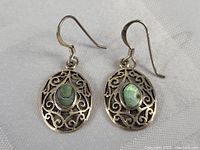 Pair of oval sterling silver earrings with intricate scroll filigree and oval abalone shell centers, shown on a textured white background.