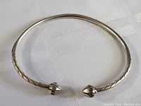 Sterling silver cuff bracelet laid flat on a white textured fabric background, showing the decorative engraved ends and pattern on the band