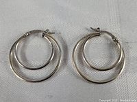 Pair of sterling silver earrings shown flat side by side on fabric background, clear view of double hoop design and post backs.