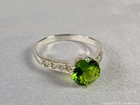 Photo showing sterling silver ring with bright green central stone and clear accents on band, angled to highlight stone and band detail.