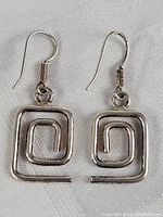 Pair of silver-toned maze design earrings with hooks on a white textured fabric background. Both earrings shown from slightly different angles to highlight the design and condition.